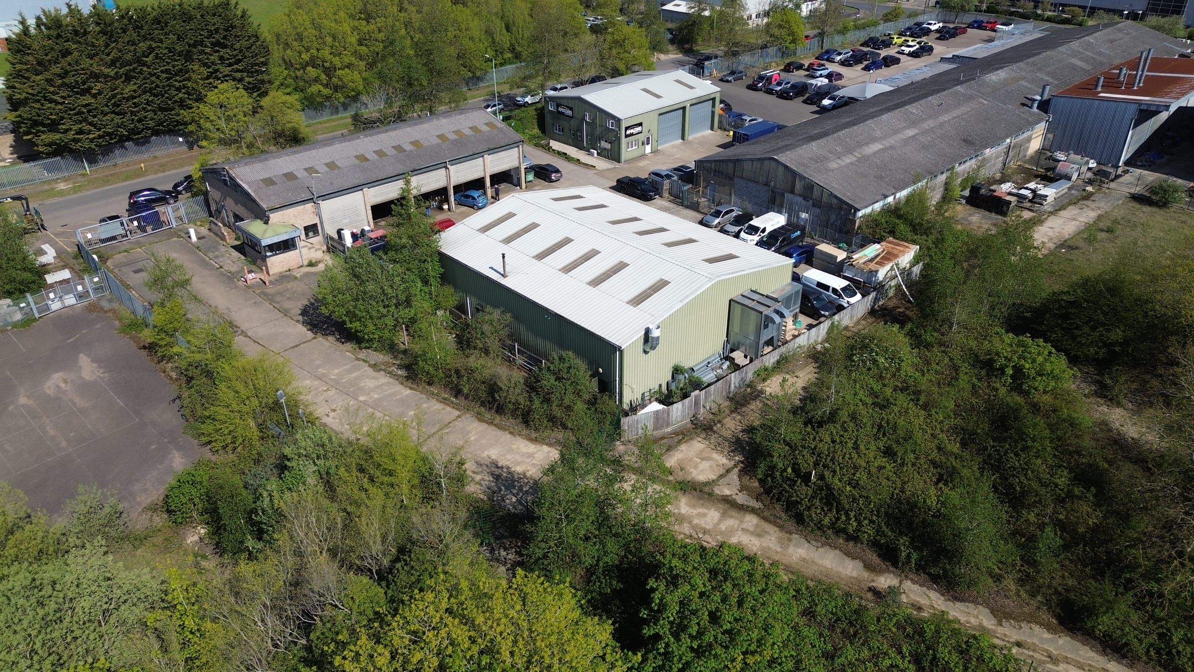 Aerial drone view of industrial warehouse units surrounded by trees