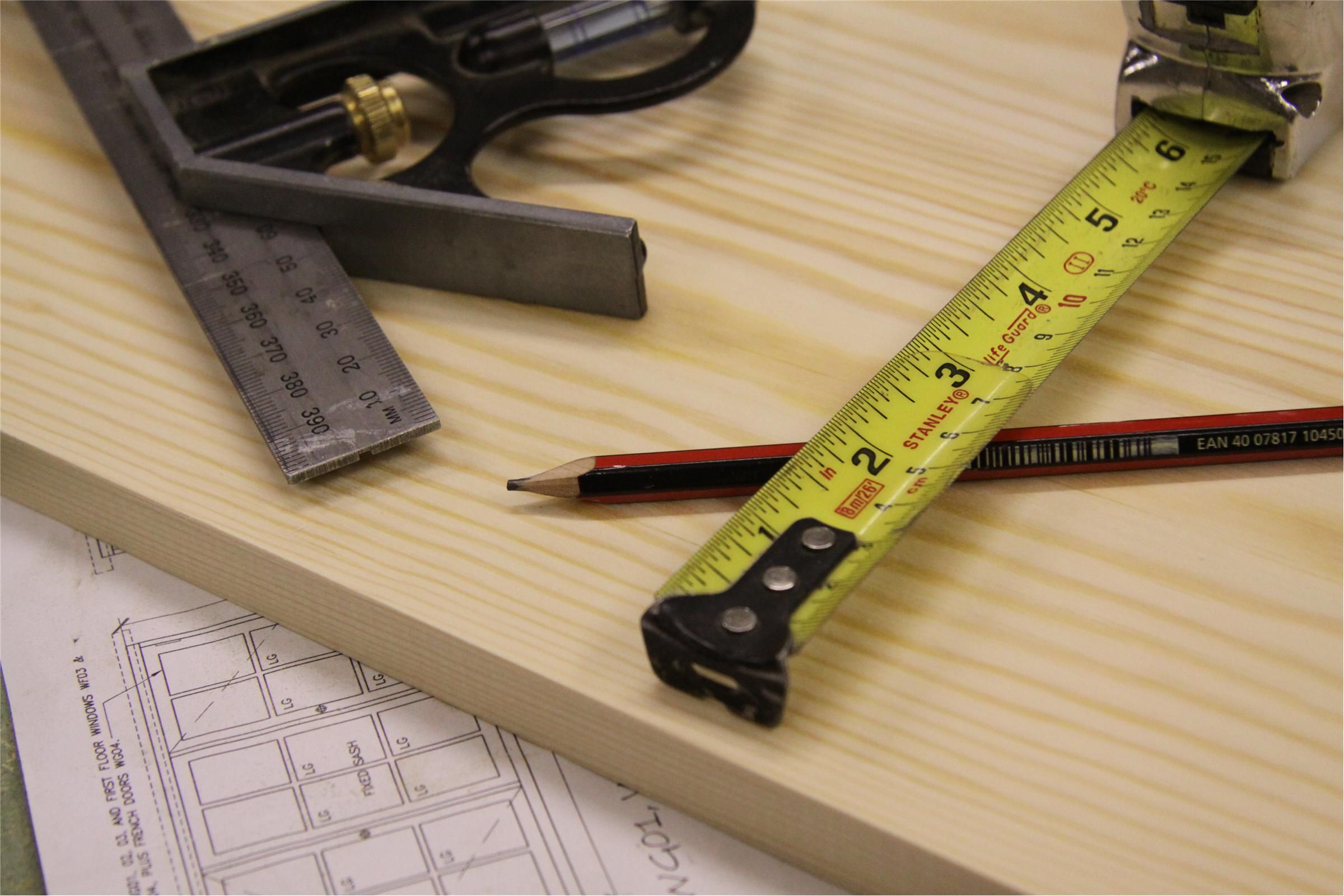 Tape measure, pencil and try square laid on timber over building plans