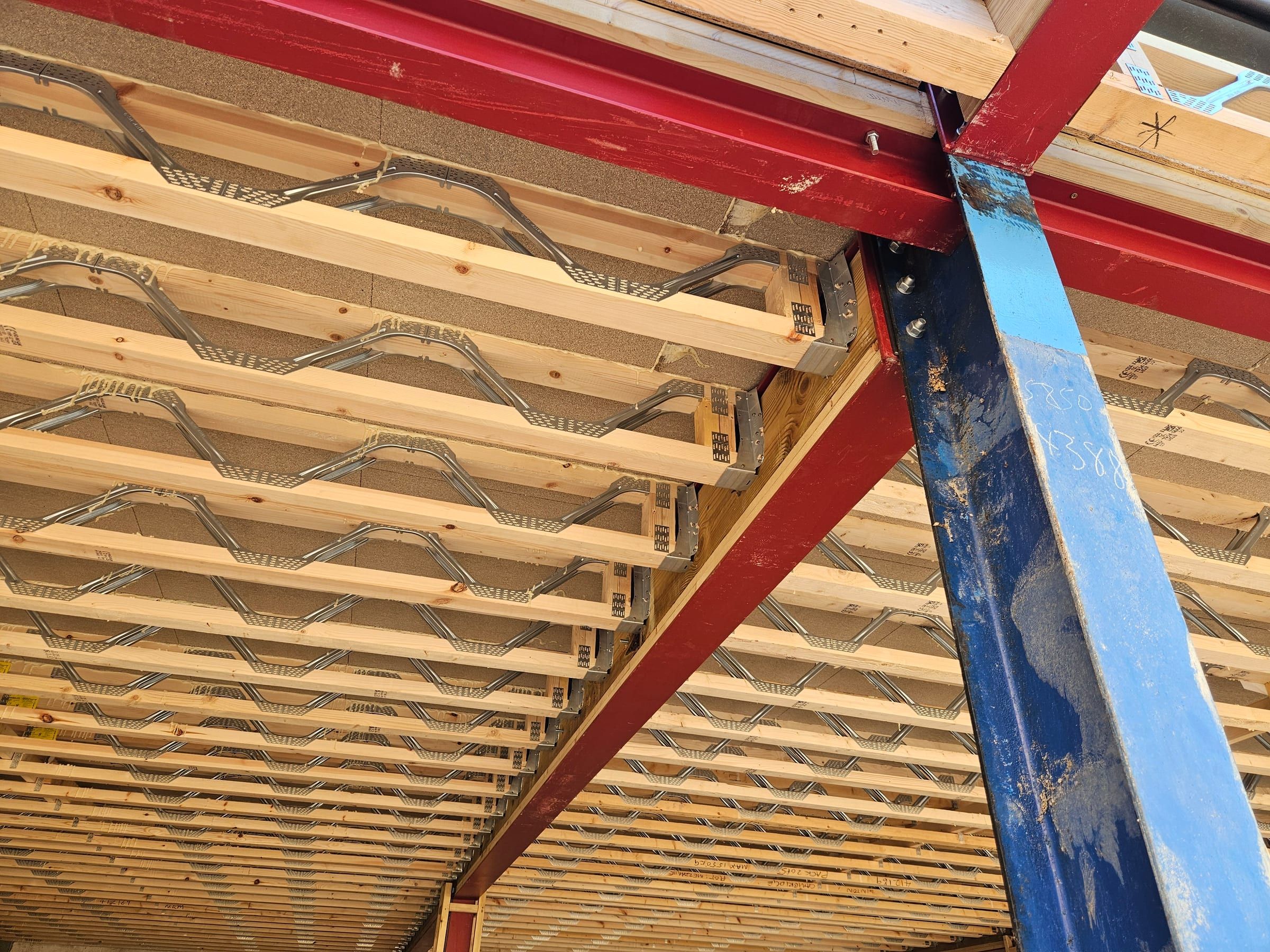 Timber roof joists with metal web trusses meeting a steel structural beam