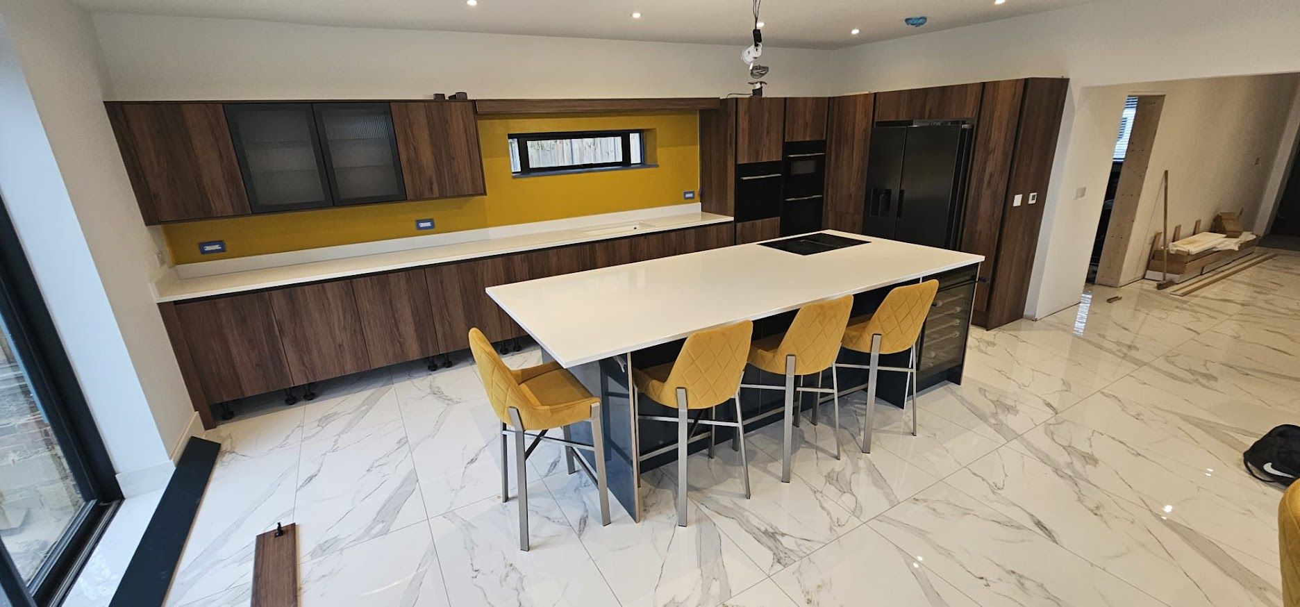 Finished kitchen with dark cabinetry, mustard splashback and island with bar stools