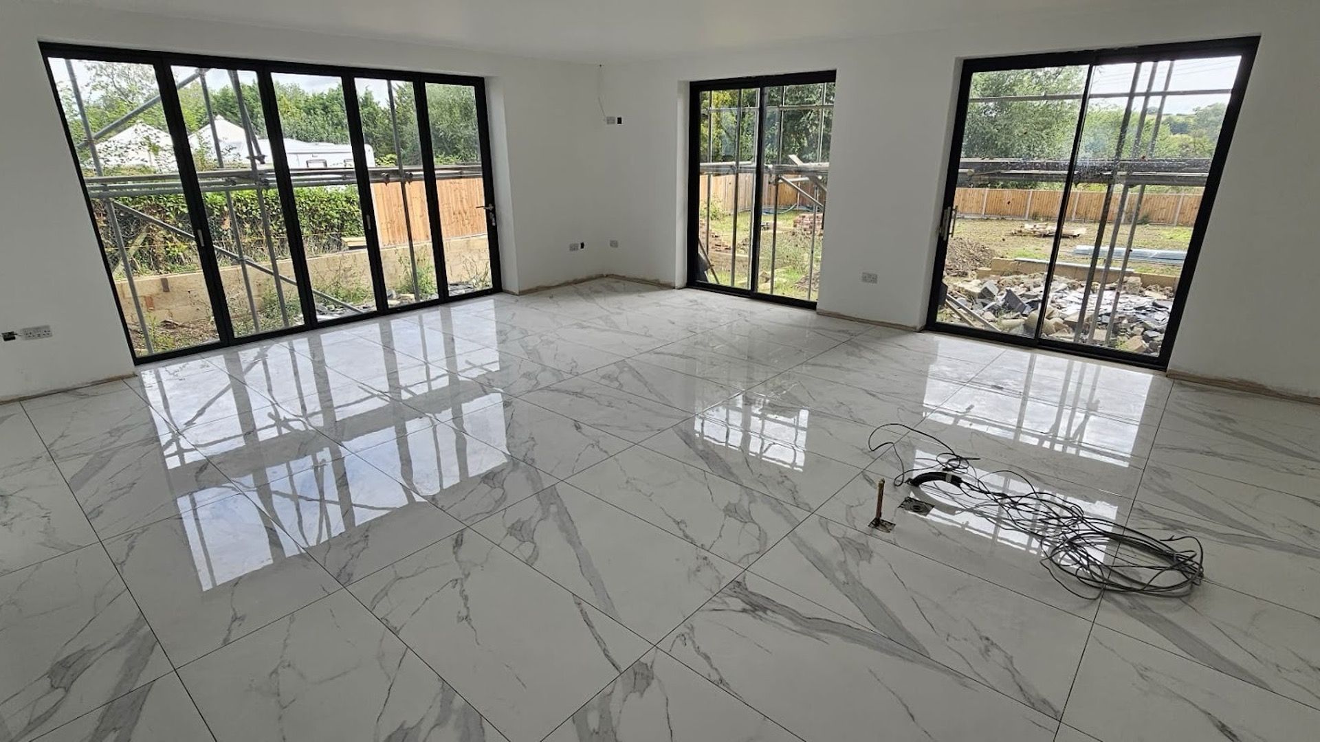 Open-plan room mid-fit-out with large marble-effect floor tiles and bi-fold doors