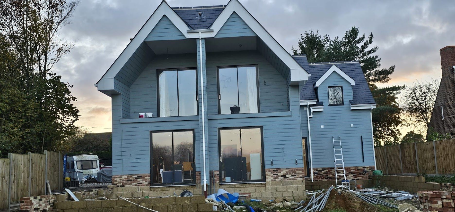 Rear of new build with full-height glazed gable and grey cladding at dusk