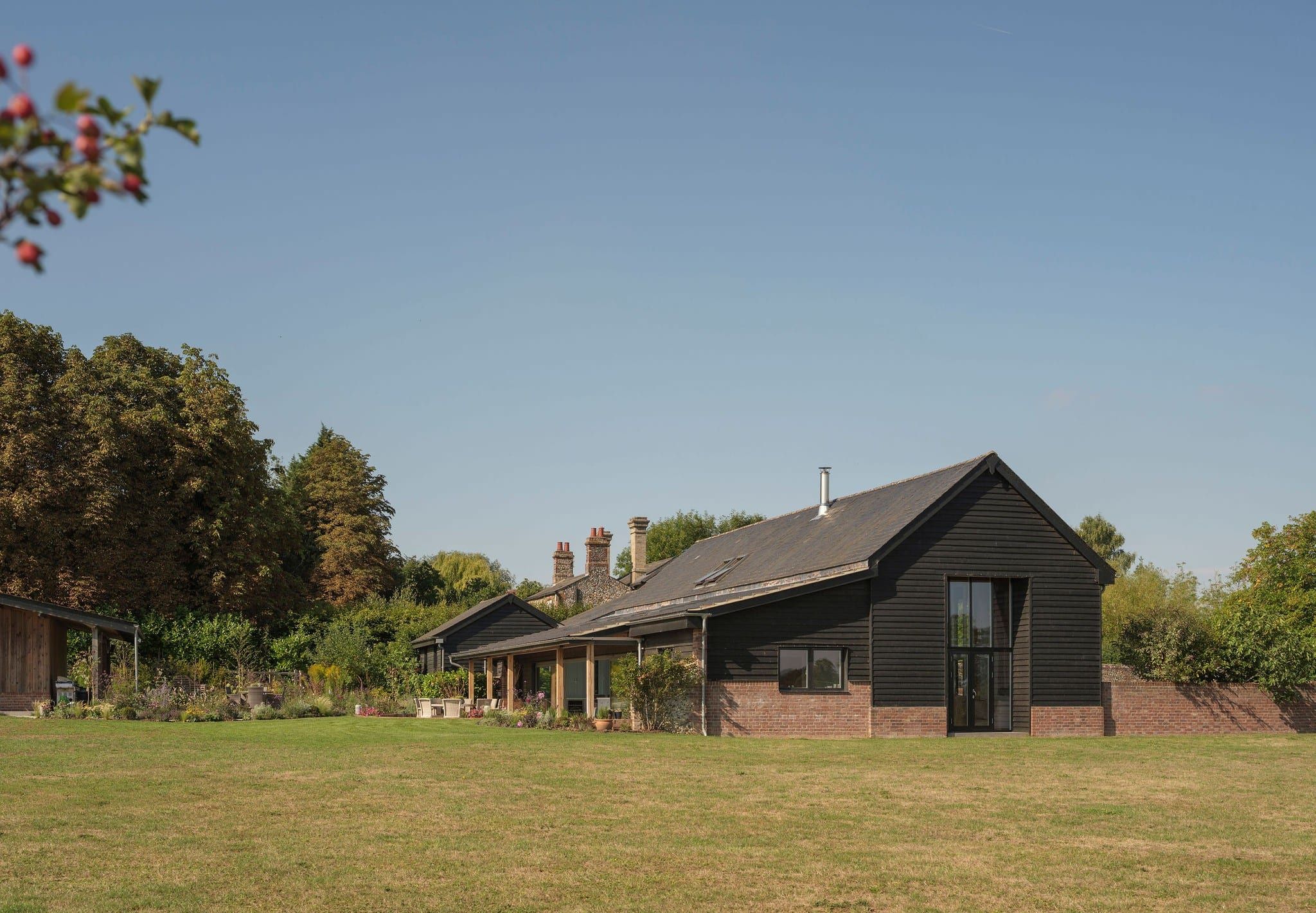 Black timber-clad barn conversion with brick base and landscaped garden