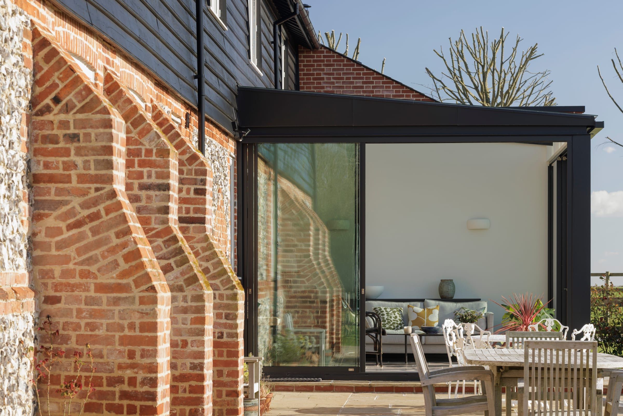Glazed garden room extension beside a buttressed brick wall, opening onto a patio