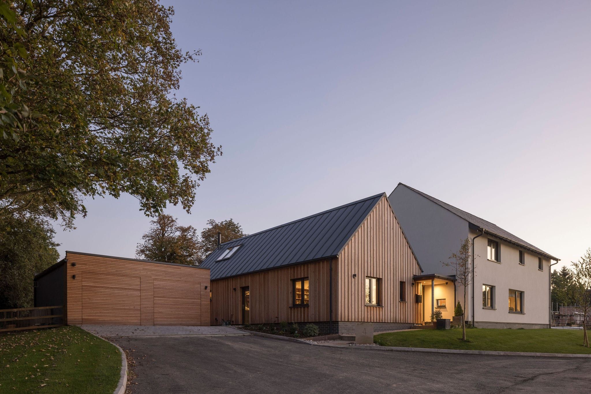Vertical timber-clad house and garage with a standing-seam roof at dusk