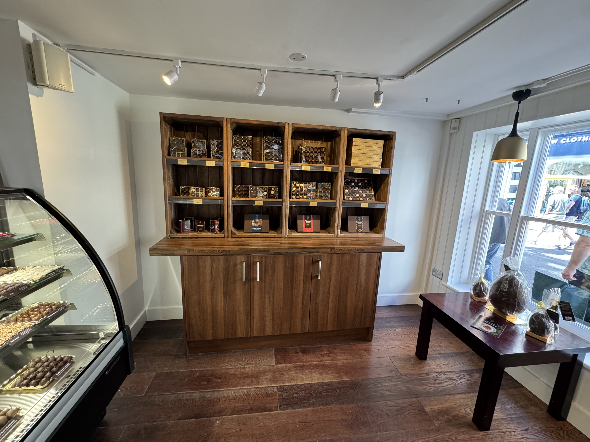 Wooden pigeonhole shelving and walnut counter beside curved glass chocolate display cabinet