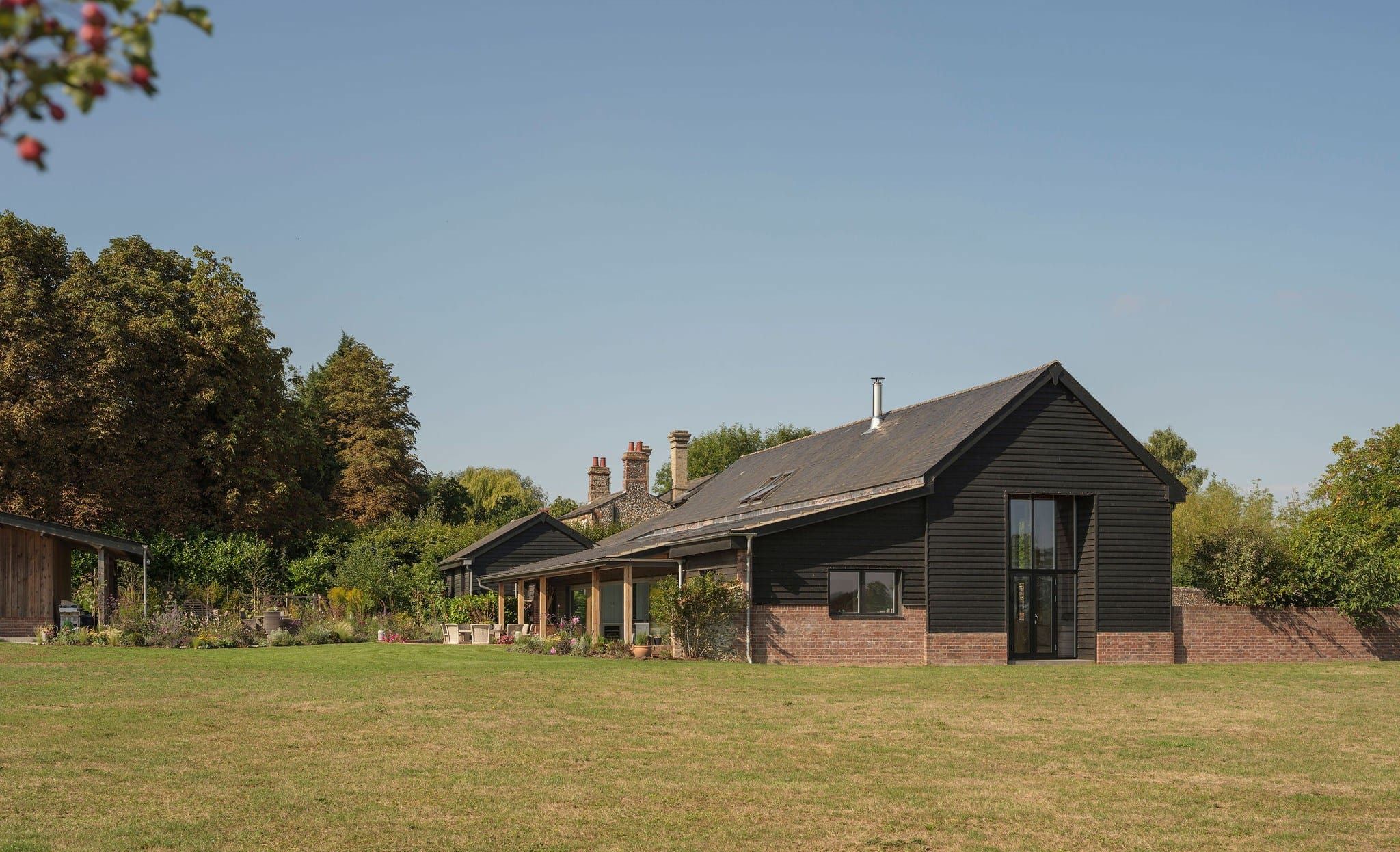 Black weatherboarded barn with a full-height glazed gable, seen across a lawn