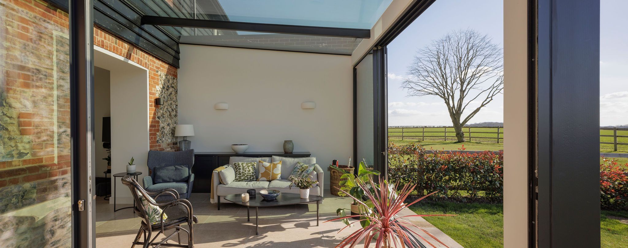 Glazed garden room with sofa and armchair, doors open to the lawn and countryside