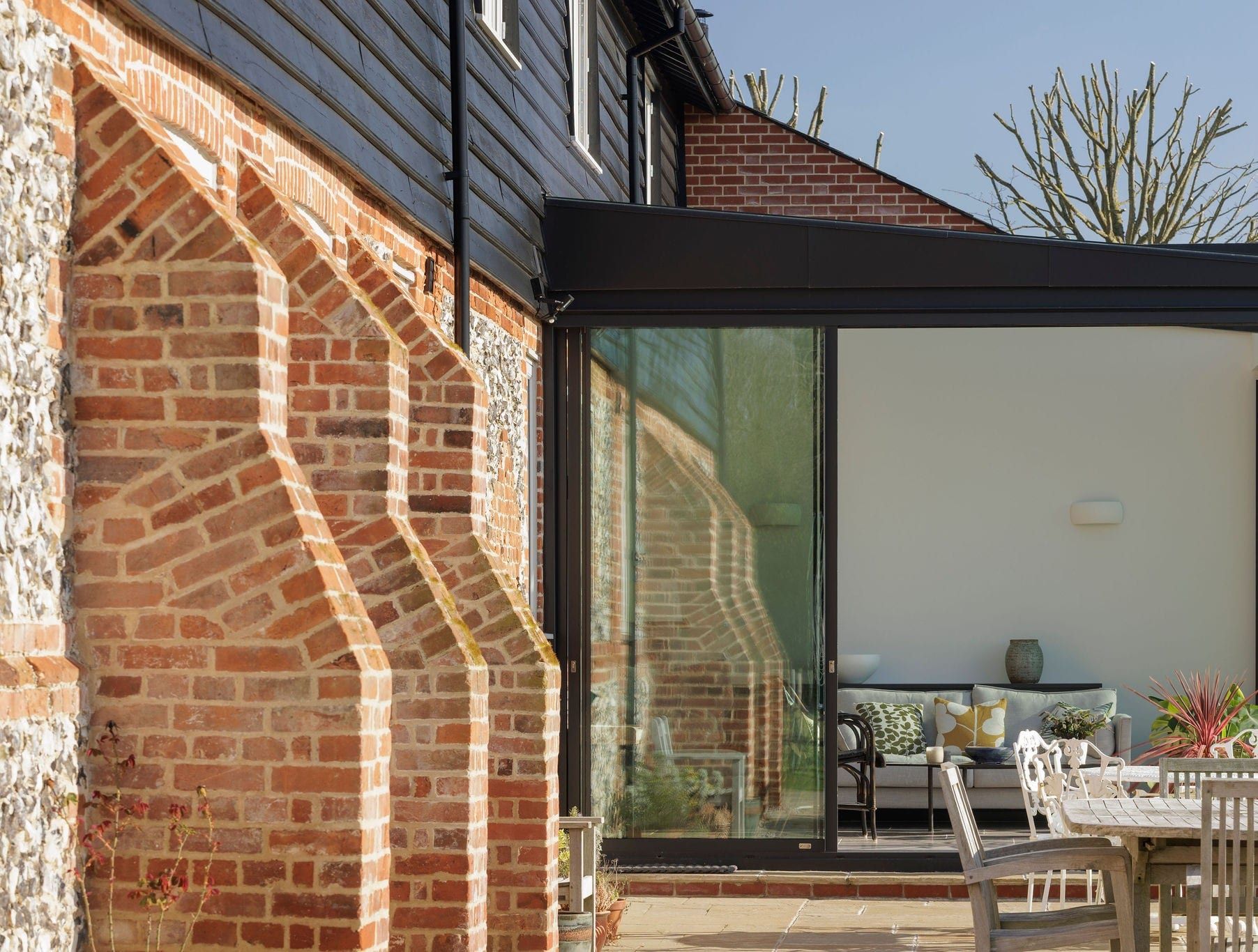 Glazed garden room beside a buttressed brick wall, with patio table and chairs