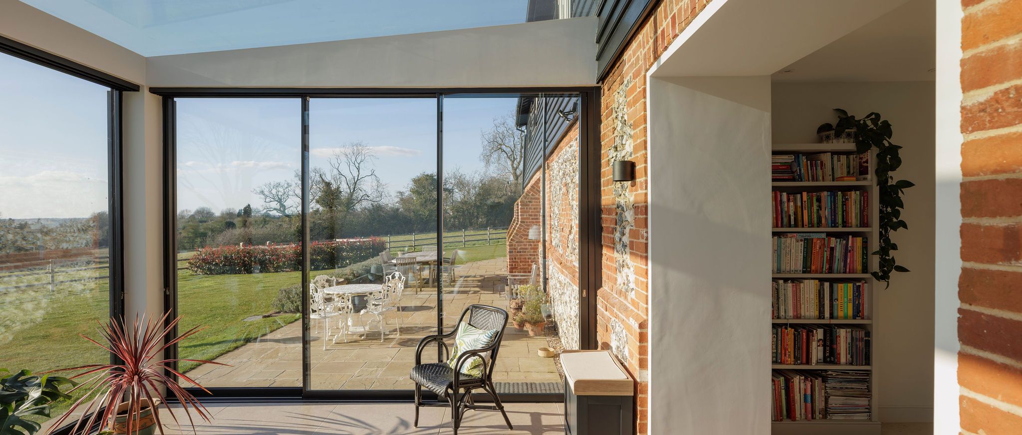 Glazed garden room with bookshelves and a brick and flint wall, looking out to the patio