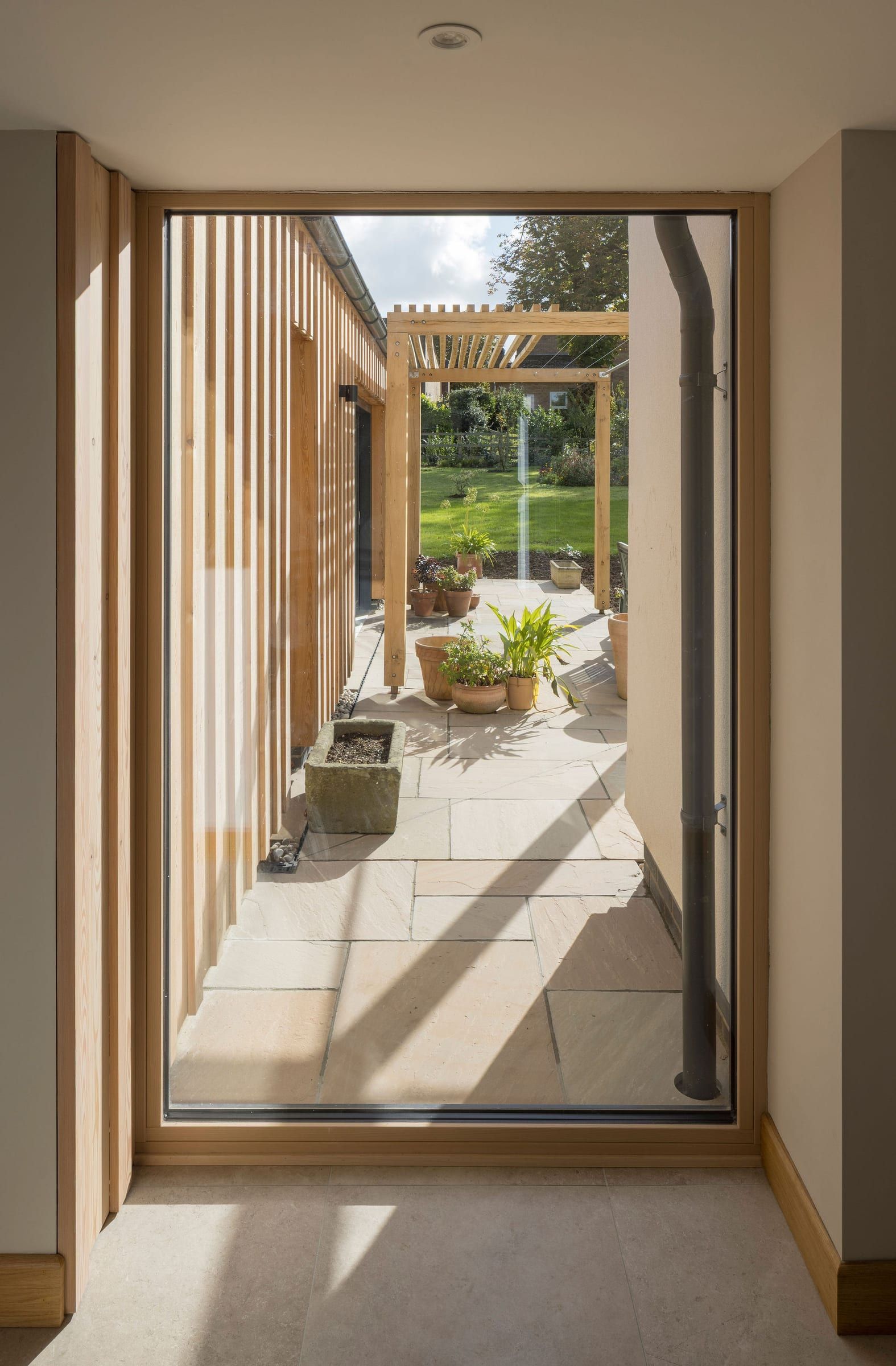 Full-height window looking onto a paved courtyard with an oak pergola