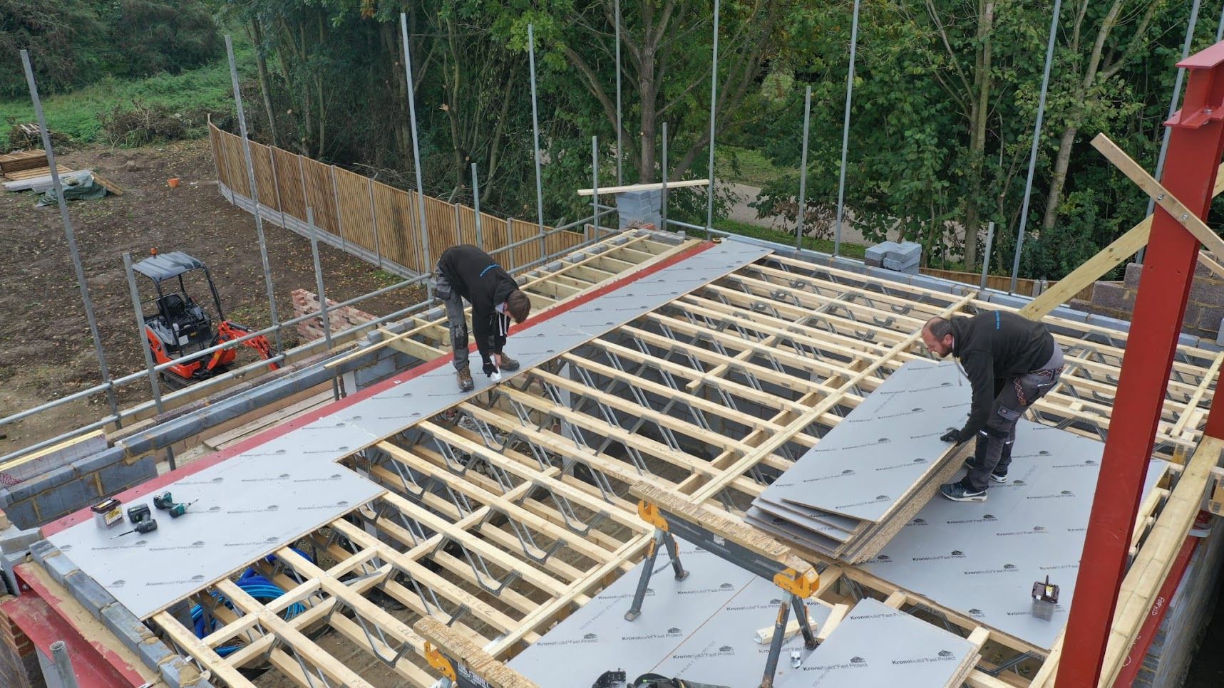 Builders fitting roof deck boards onto timber roof trusses
