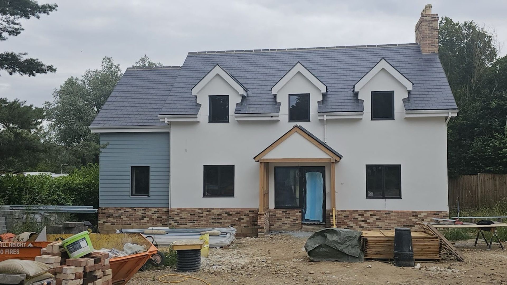 Rendered new build house with three dormer windows and an oak porch, nearing completion