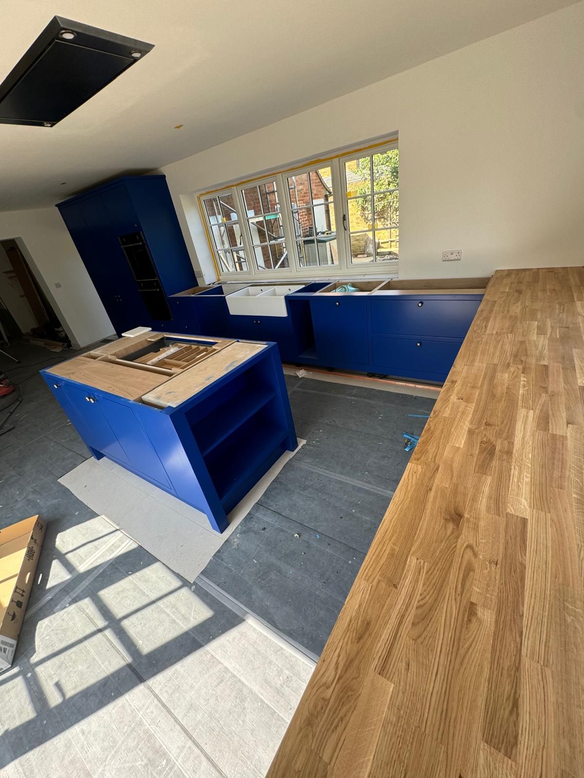 Navy blue kitchen units and island mid-installation with oak worktop