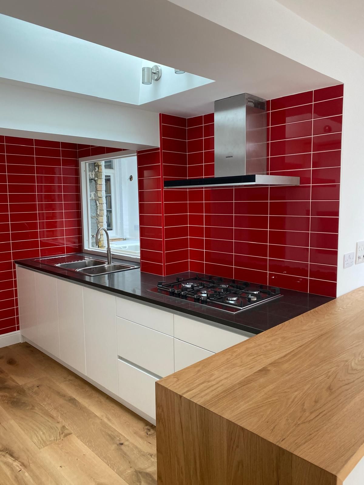 Renovated kitchen with red tiled splashback, black worktop and gas hob