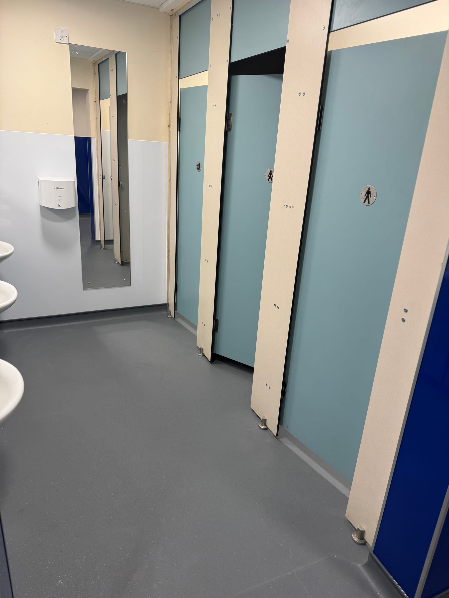 Row of new toilet cubicles with teal doors in refurbished school bathroom