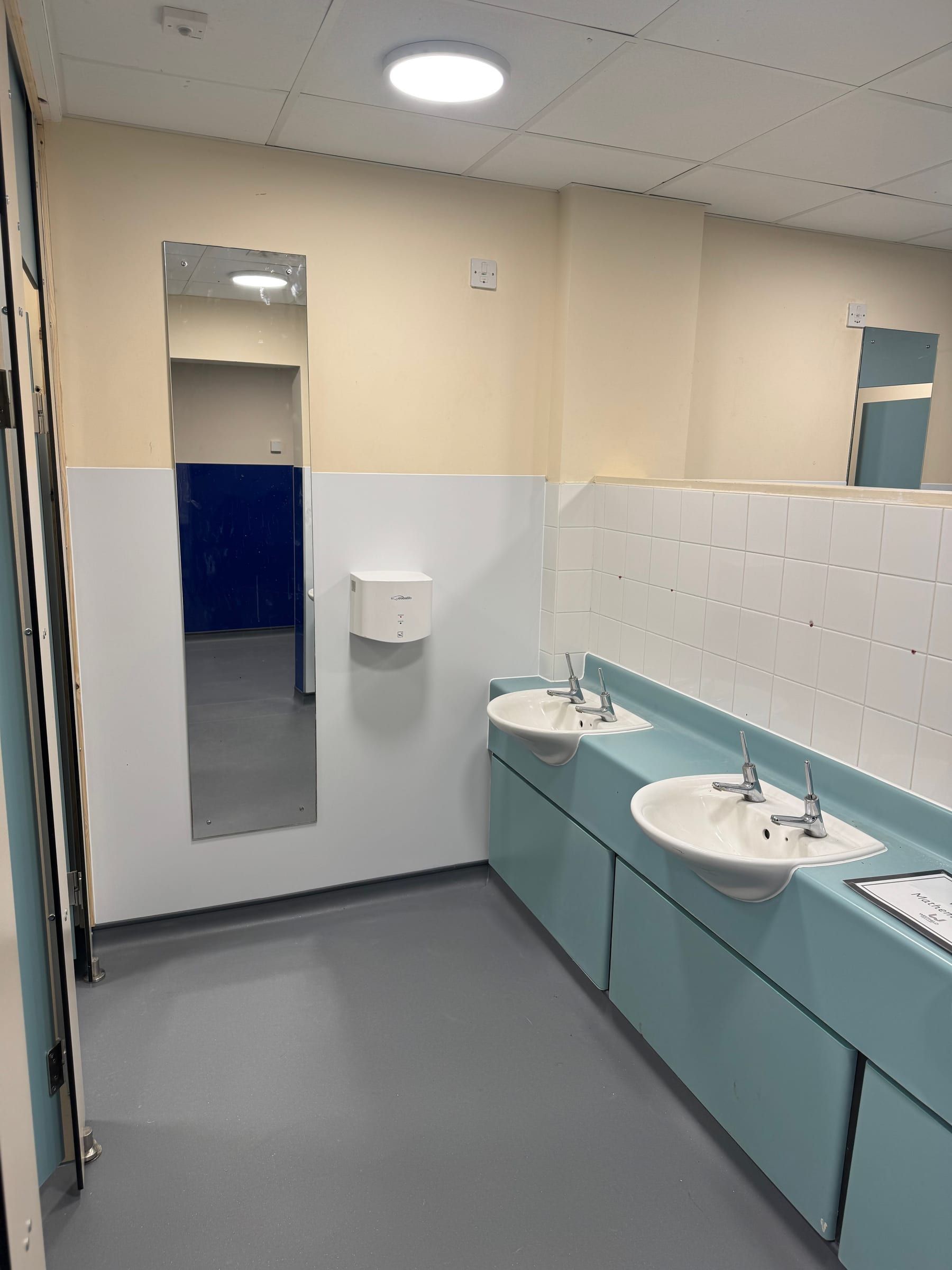 Refurbished children's bathroom with twin sinks on teal vanity unit and tiling