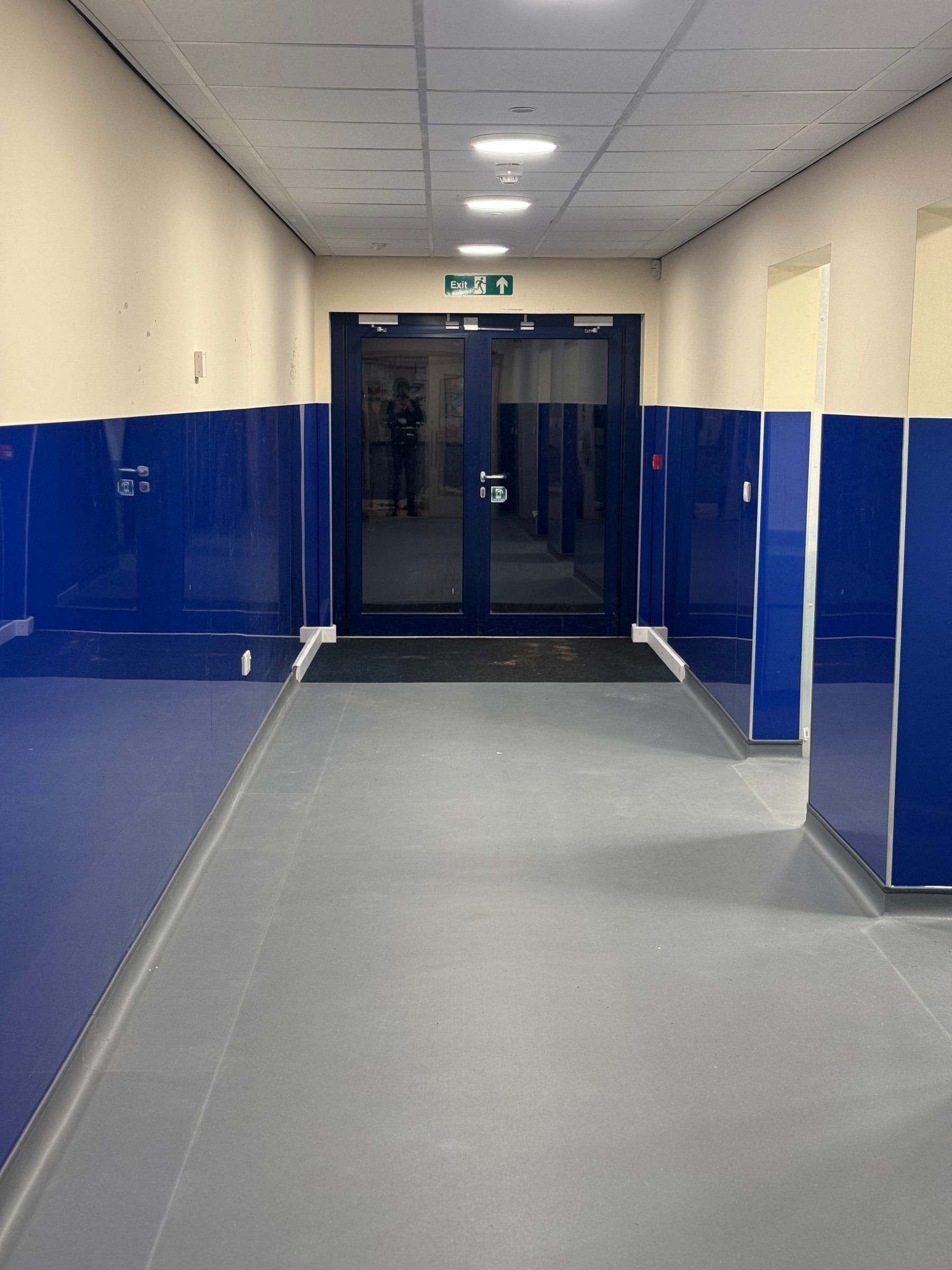 Refurbished school corridor with blue wall panelling leading to fire exit doors